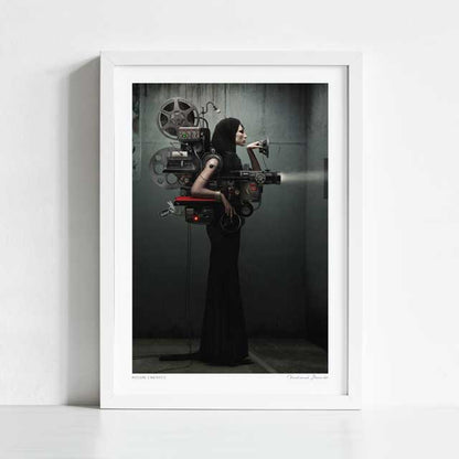 Madame Cinematic art print framed view — surreal dark fashion collage of a hooded woman as a vintage cinema projection machine with film reels and projector lens against industrial concrete, steampunk noir wall art for home cinemas and gallery walls