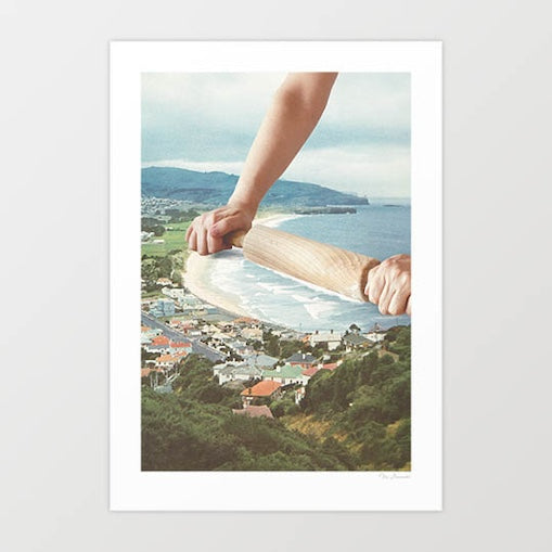 Surreal art print — giant hands rolling a wooden rolling pin across a New Zealand coastal town and harbour, flattening the ocean waves like pastry dough, aerial seaside baking wall art by Vertigo Artography